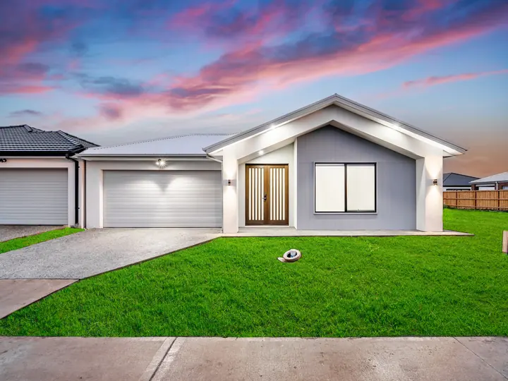 Gable facade with a double garage and a timber entry door, lit at dusk, in a single-storey home Oakview built in Clyde North