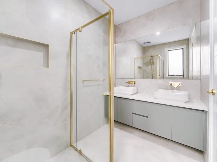 Ensuite with a gold-framed shower and double vanity, in a custom home Oakview finished in brushed gold fittings