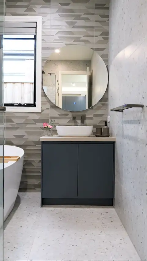 Moving view of a vessel basin under a round mirror, beside a freestanding bath, in a Clyde North home built by Oakview Homes